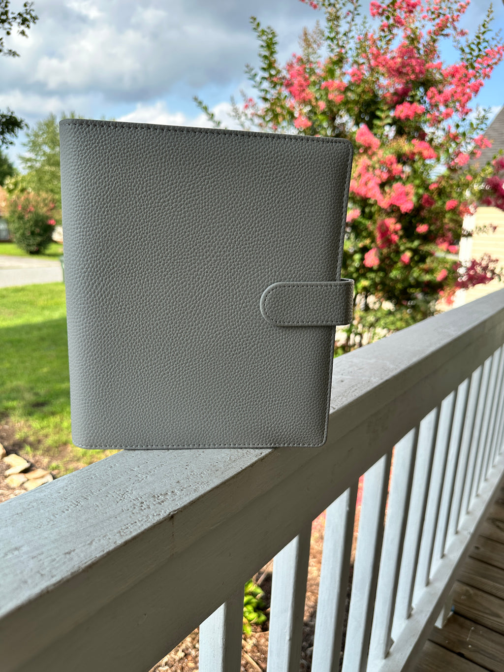 A light gray pebbled leather binder with side strap snap closure.